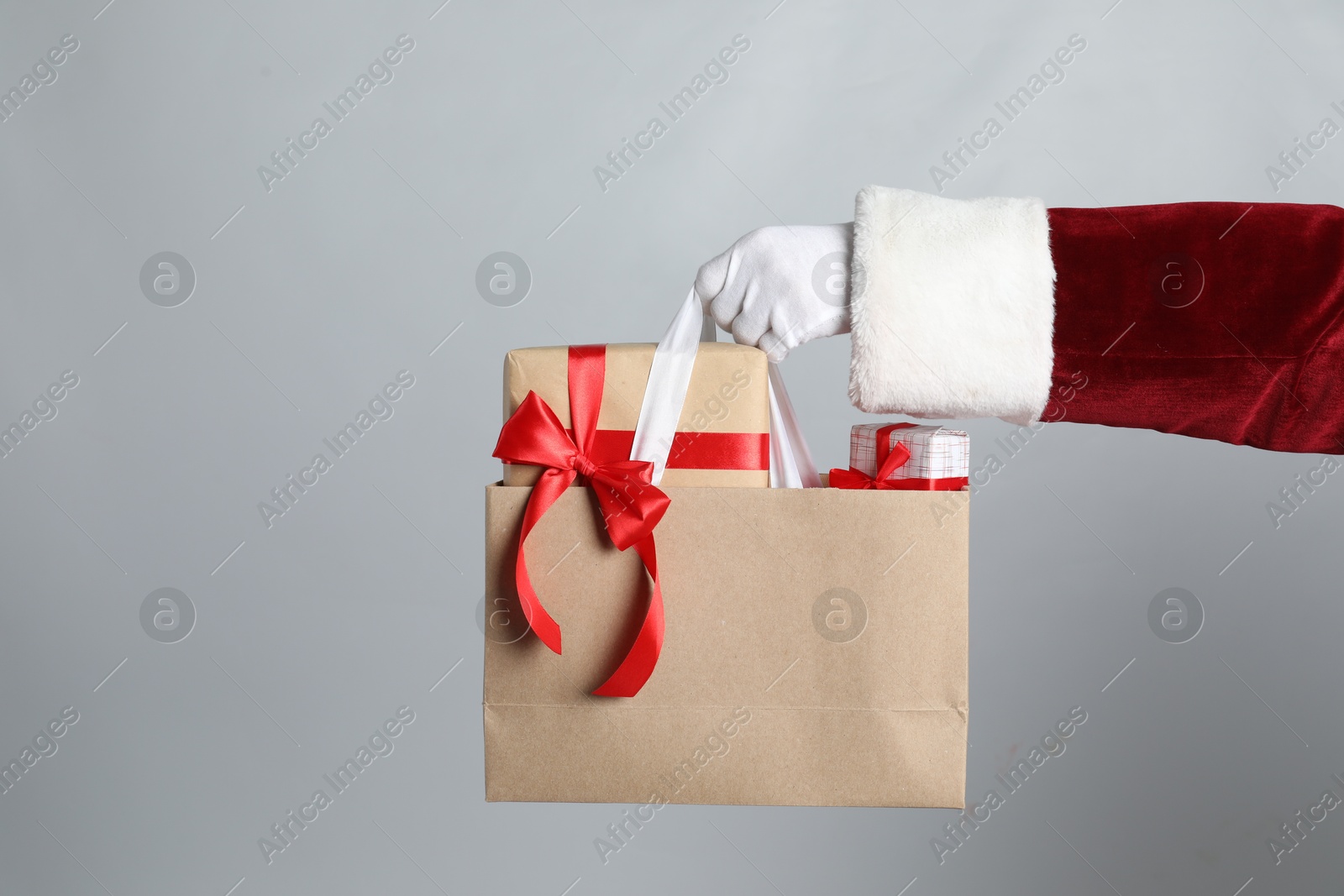 Photo of Santa holding paper bag with gift boxes on light grey background, closeup