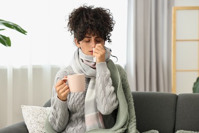 Photo of Cold symptom. Young woman with tissue and cup of hot drink at home