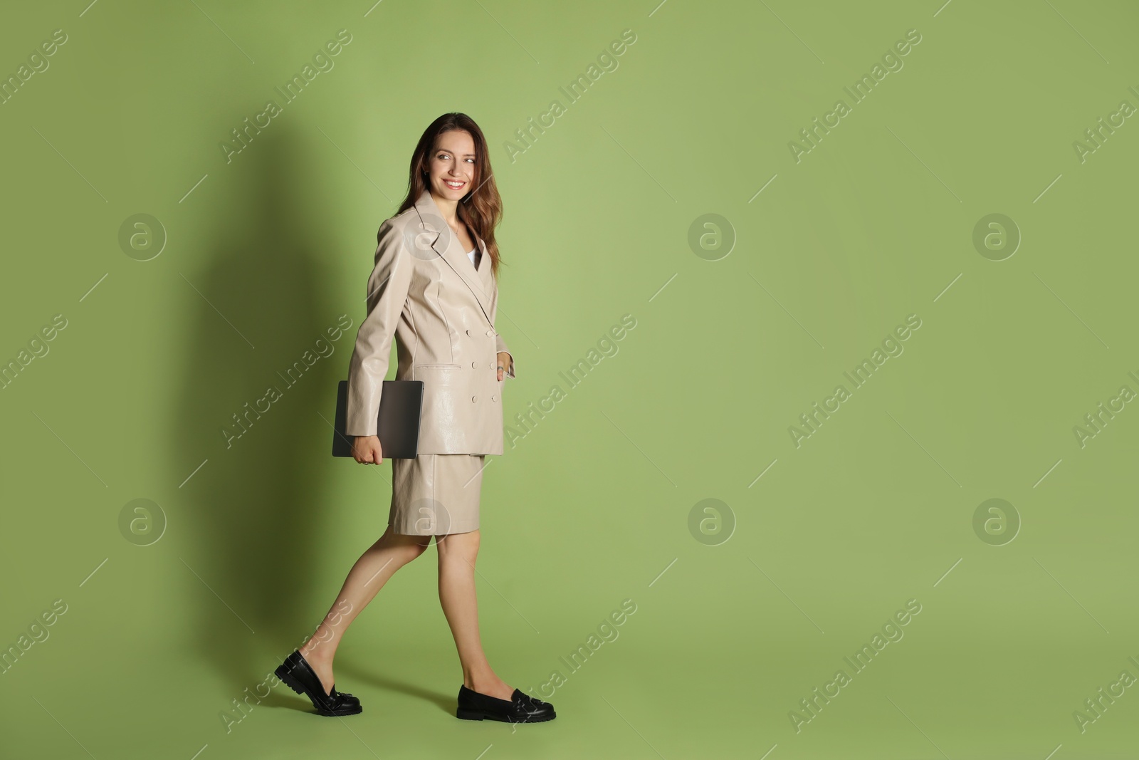 Photo of Beautiful woman in stylish beige suit with laptop on olive background, space for text