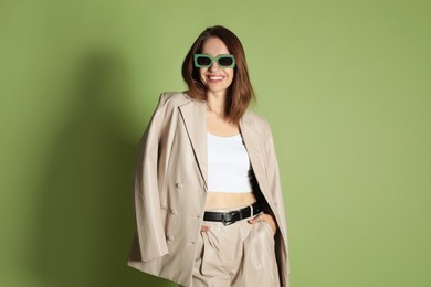 Photo of Beautiful woman in stylish beige suit and sunglasses on olive background