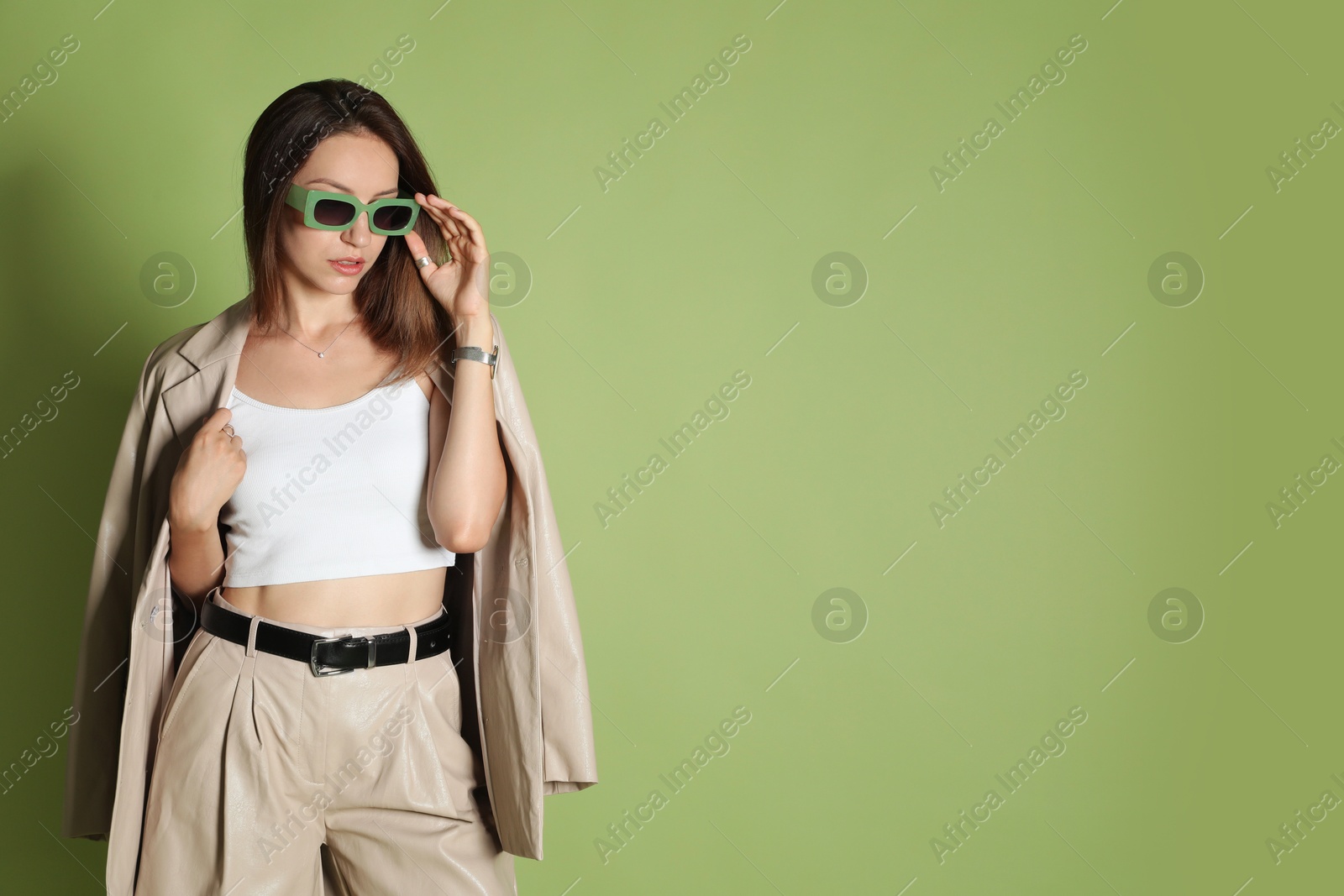 Photo of Beautiful woman in stylish beige suit and sunglasses on olive background, space for text