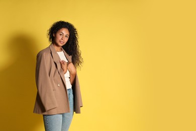 Beautiful woman with stylish jacket on yellow background, space for text