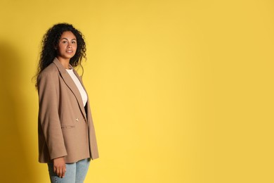 Beautiful woman in stylish jacket on yellow background, space for text