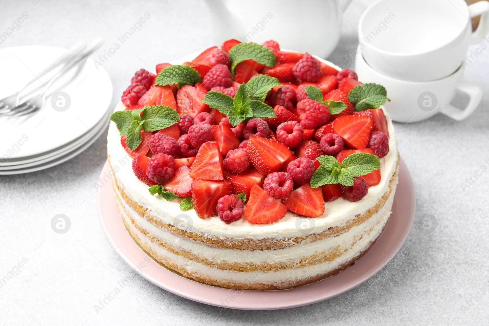 Photo of Tasty sponge cake with fresh berries and mint on light gray table