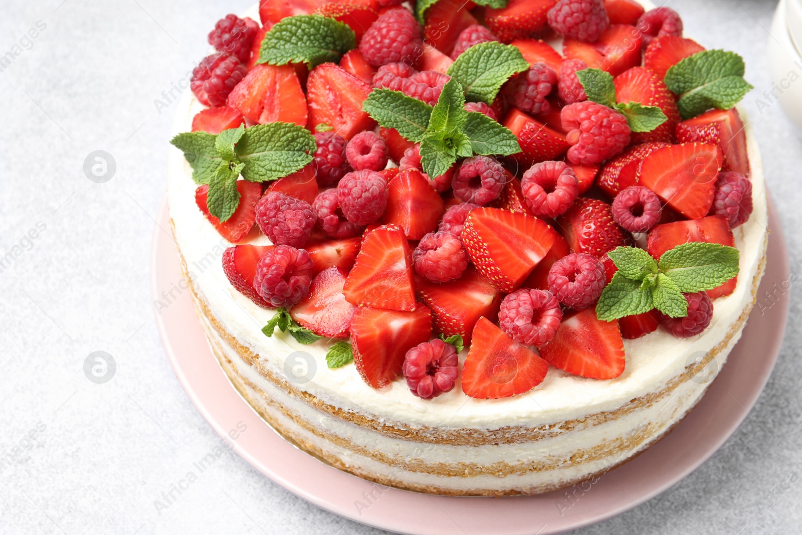 Photo of Tasty sponge cake with fresh berries and mint on light gray table, closeup