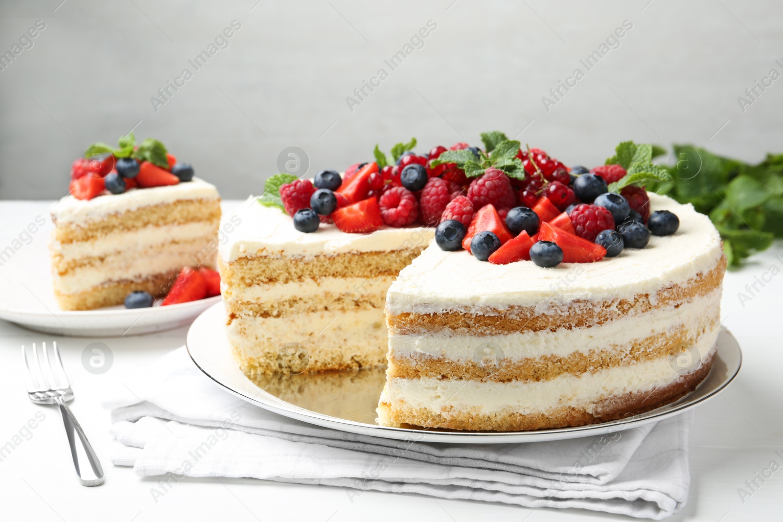 Photo of Tasty sponge cake with fresh berries and mint served on white table