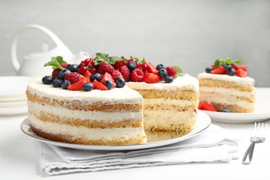 Photo of Tasty sponge cake with fresh berries and mint served on white table