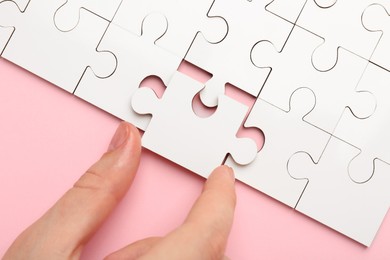 Photo of Woman solving white puzzle on pink background, closeup