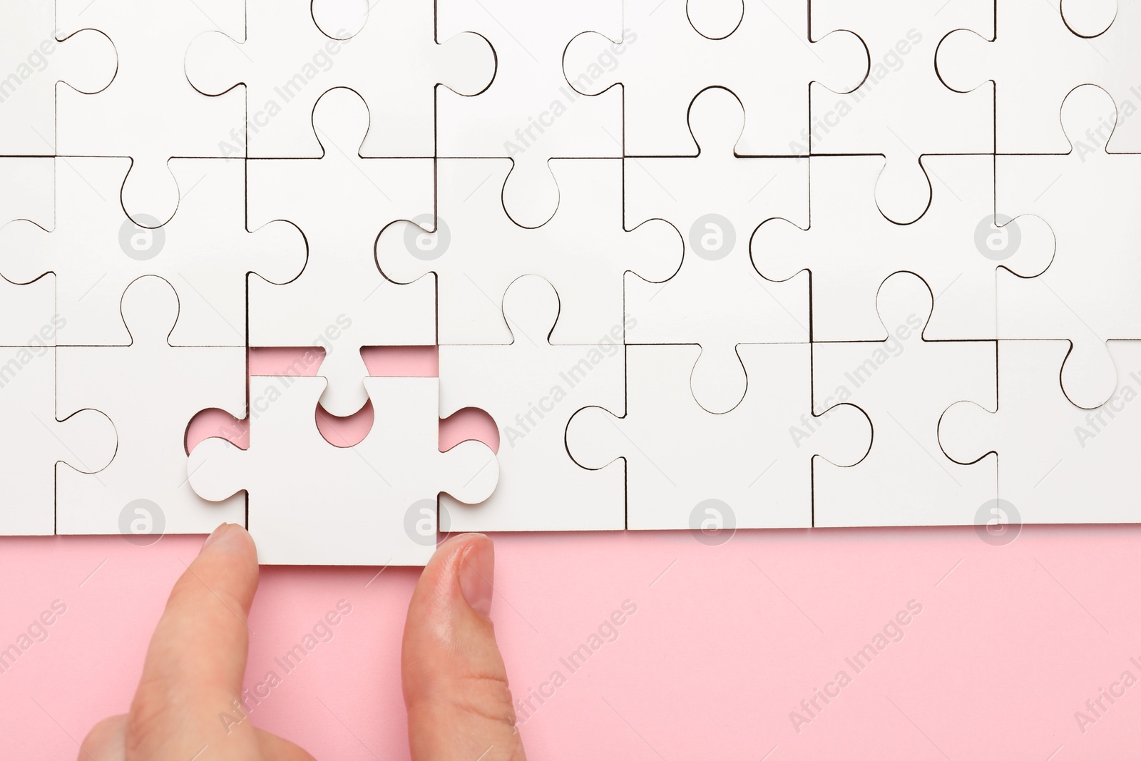 Photo of Woman solving white puzzle on pink background, closeup