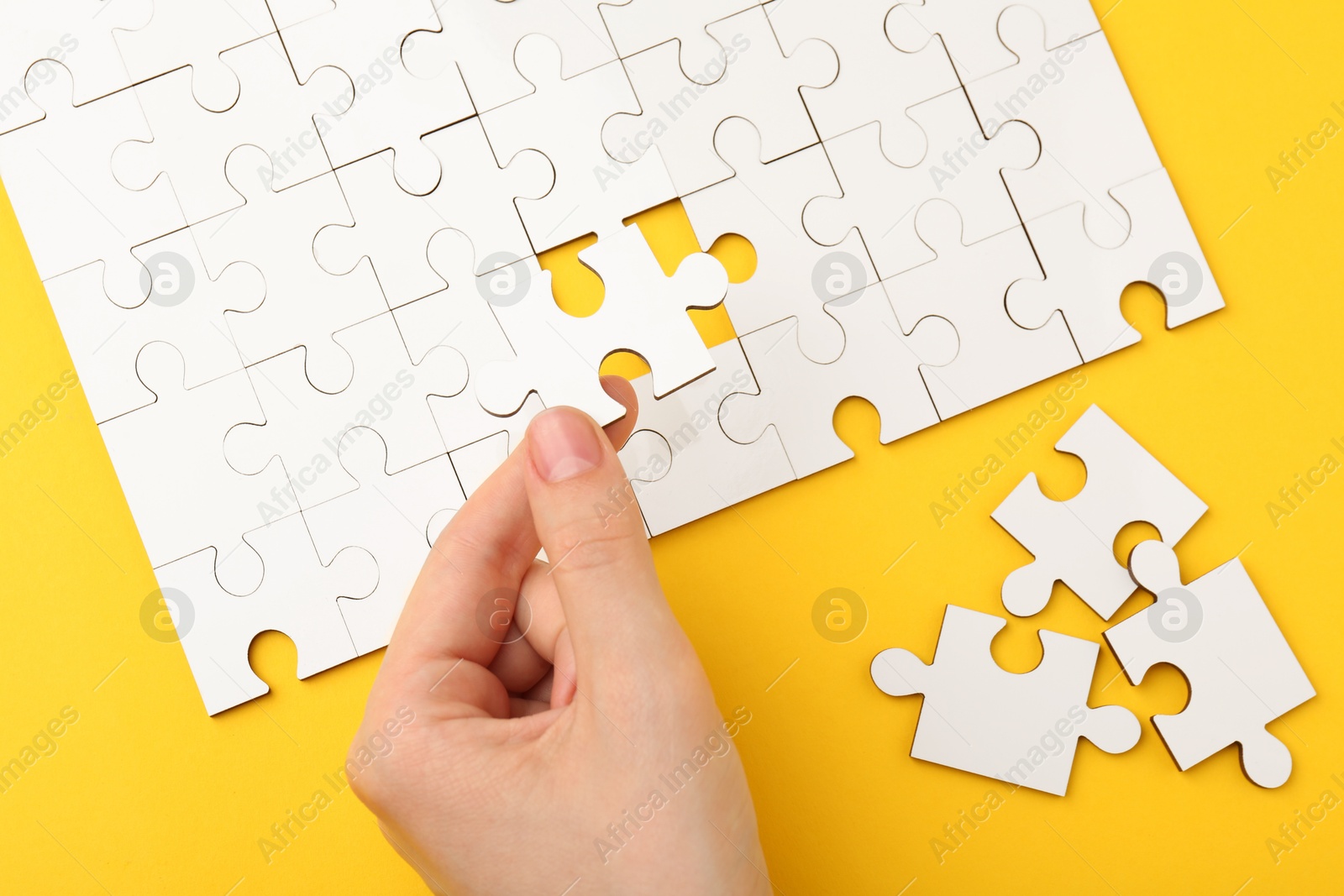 Photo of Woman solving white puzzle on yellow background, closeup