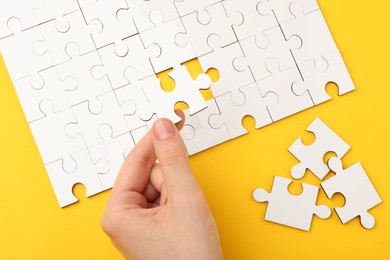 Photo of Woman solving white puzzle on yellow background, closeup