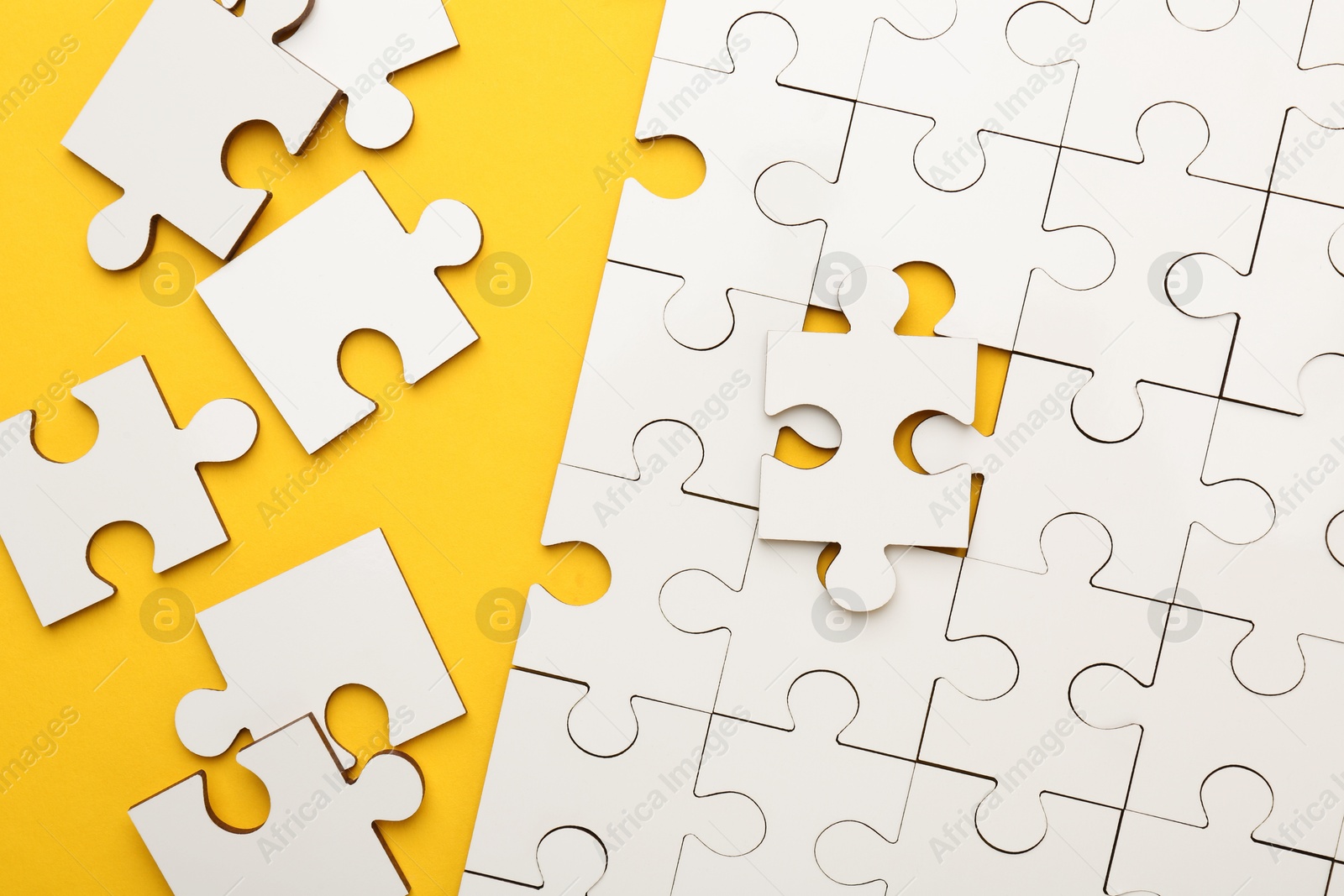 Photo of White puzzle pieces on yellow background, top view