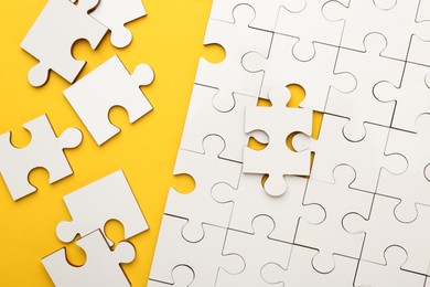 Photo of White puzzle pieces on yellow background, top view