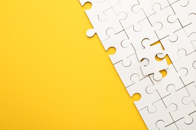 Photo of White puzzle pieces on yellow background, top view. Space for text