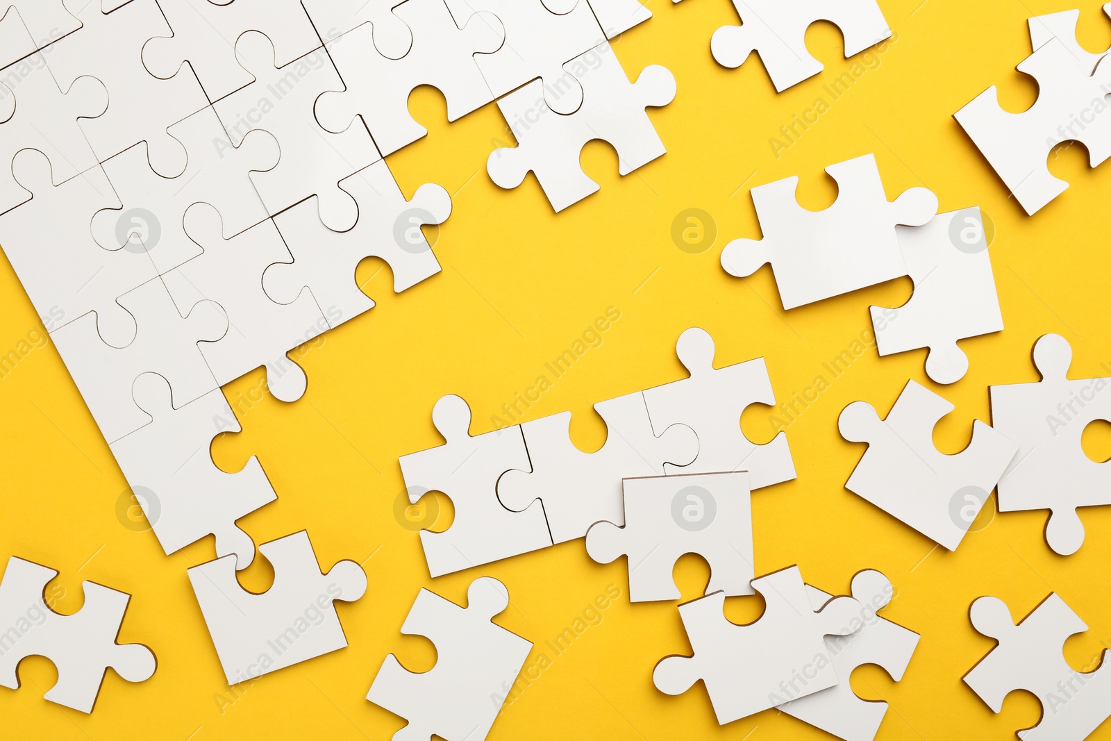 Photo of White puzzle pieces on yellow background, top view