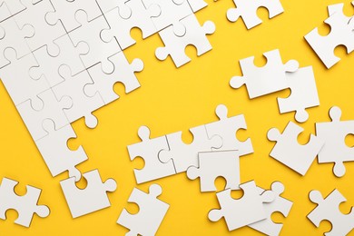 Photo of White puzzle pieces on yellow background, top view