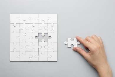 Photo of Woman solving white puzzle on light grey background, top view