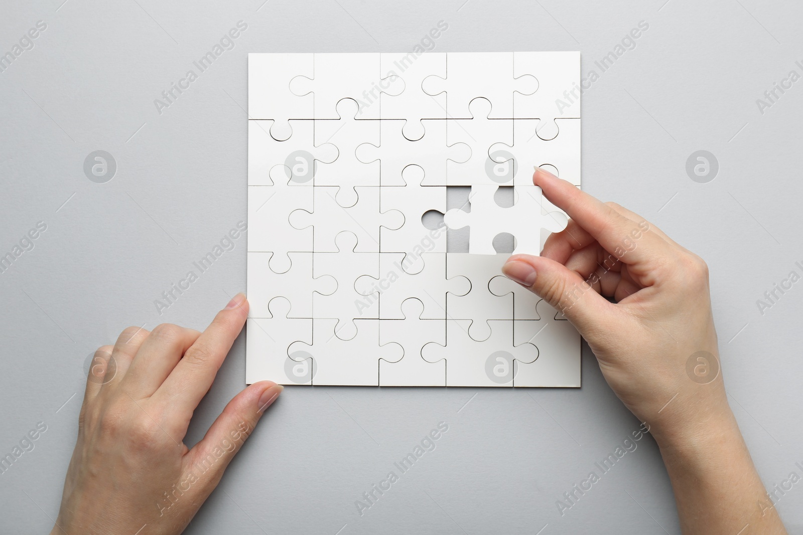 Photo of Woman solving white puzzle on light grey background, top view