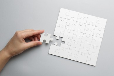 Photo of Woman solving white puzzle on light grey background, top view