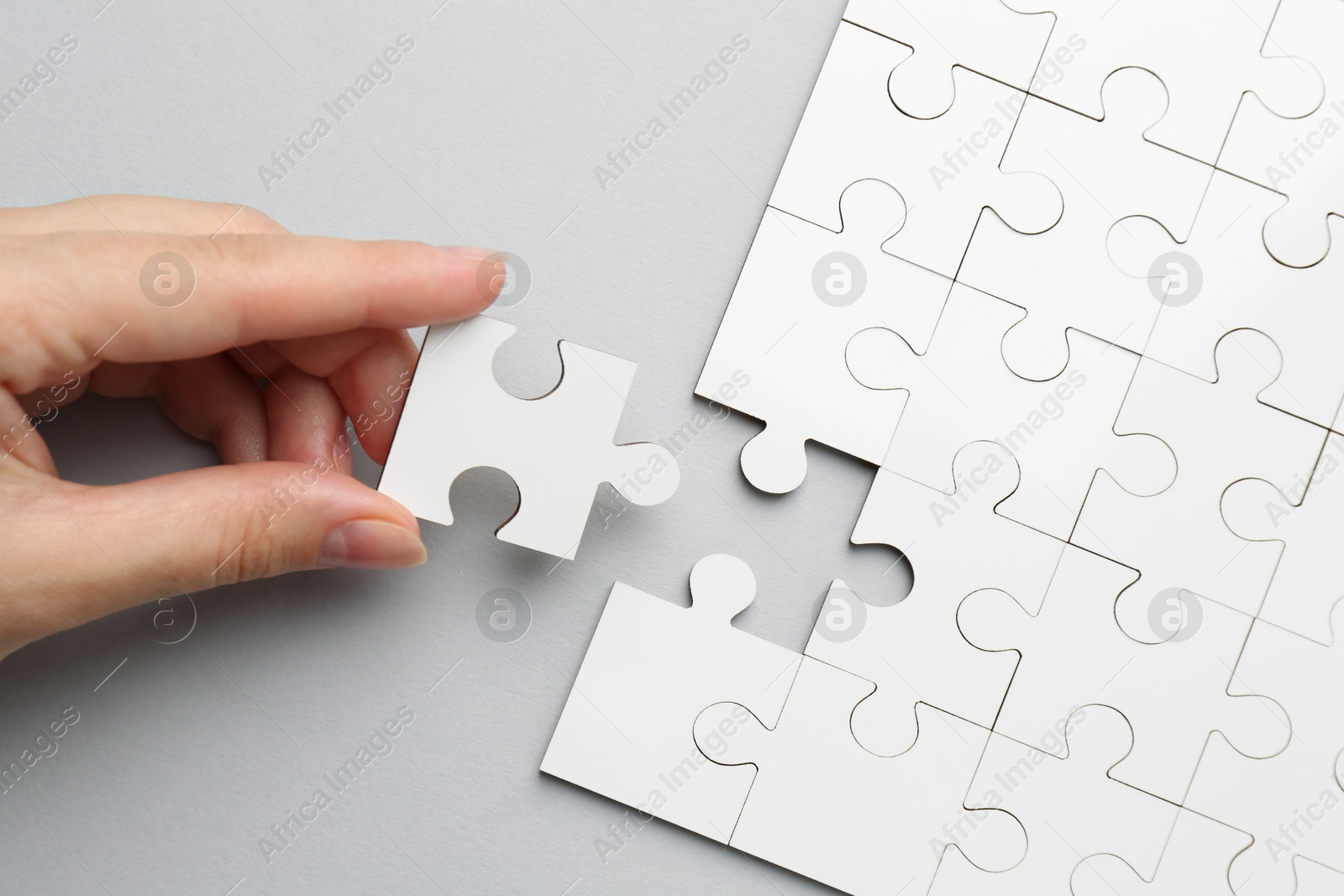 Photo of Woman solving white puzzle on light grey background, top view