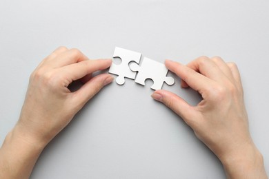 Photo of Woman solving white puzzle on light grey background, top view