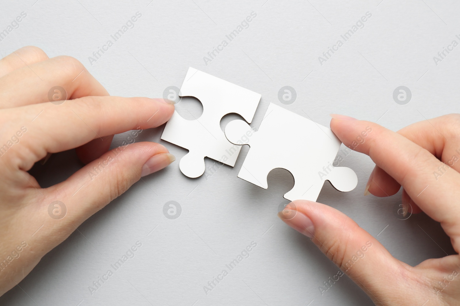 Photo of Woman solving white puzzle on light grey background, top view