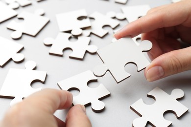 Photo of Woman solving white puzzle on light grey background, closeup