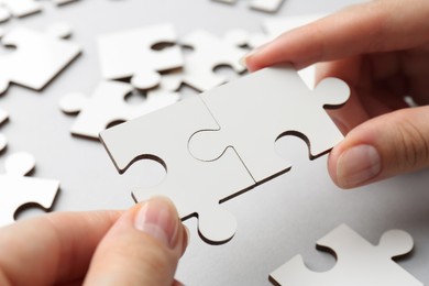 Photo of Woman solving white puzzle on light grey background, closeup