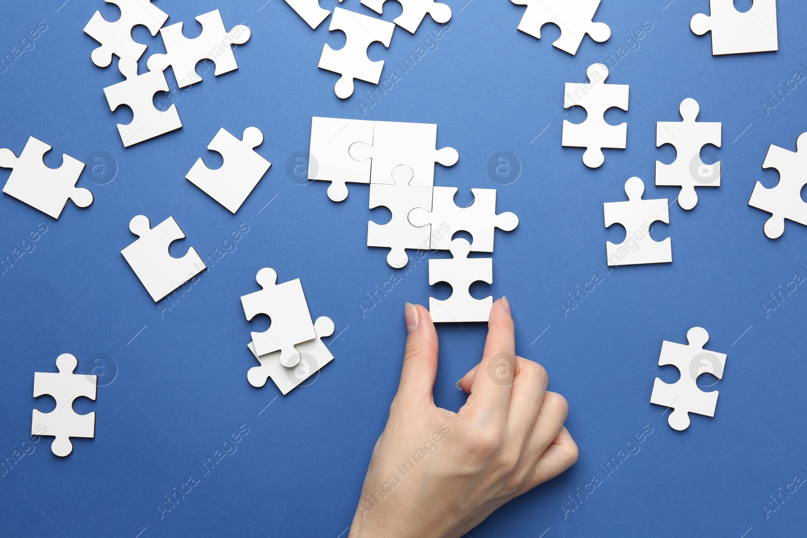 Photo of Woman solving white puzzle on blue background, top view