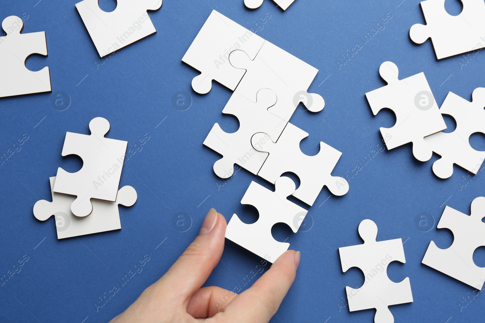 Photo of Woman solving white puzzle on blue background, top view