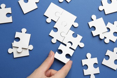 Photo of Woman solving white puzzle on blue background, top view