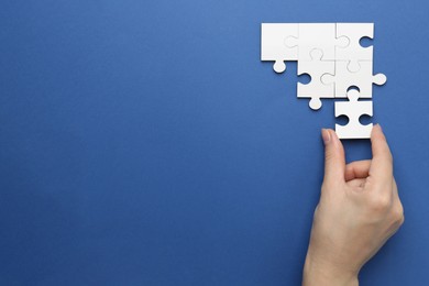 Photo of Woman solving white puzzle on blue background, top view. Space for text