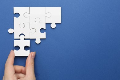 Photo of Woman solving white puzzle on blue background, top view. Space for text