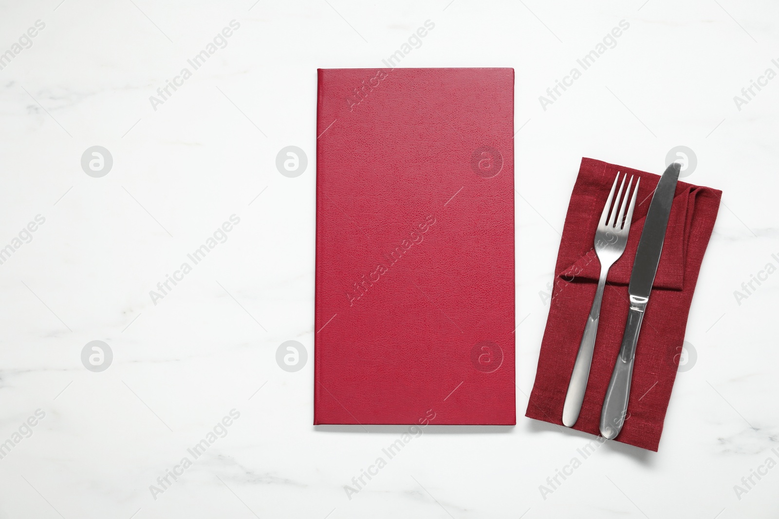 Photo of Hardcover menu and cutlery on white marble table, flat lay