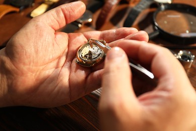 Photo of Man fixing mechanism of vintage wrist watch at wooden table, closeup