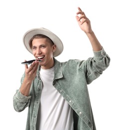 Photo of Young man in hat recording voice message via smartphone on white background