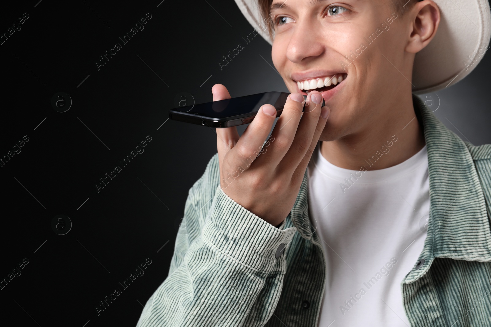 Photo of Young man recording voice message via smartphone on dark background, space for text