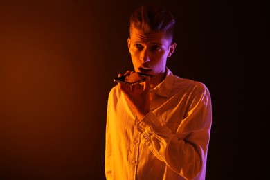 Photo of Young man recording voice message via smartphone on color background with neon lights, space for text