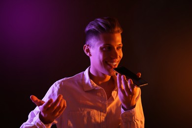 Photo of Young man recording voice message via smartphone on dark background with neon lights