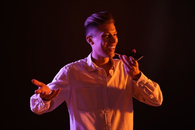 Young man recording voice message via smartphone on dark background with neon lights