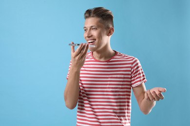 Young man recording voice message via smartphone on light blue background