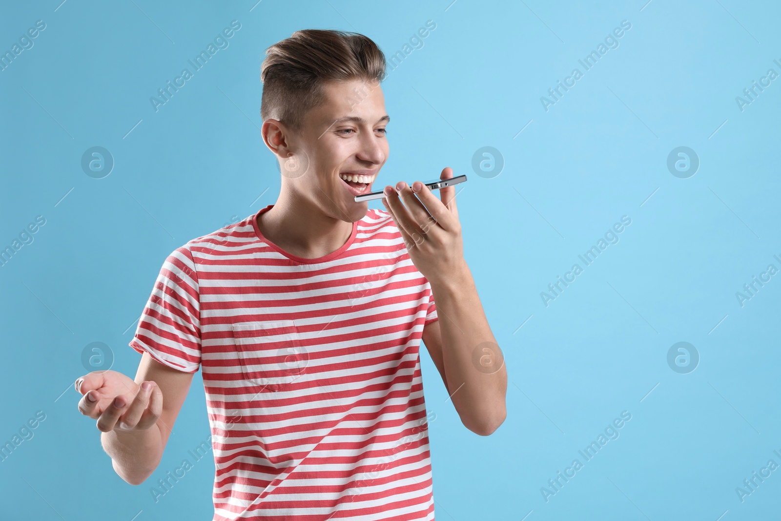 Photo of Young man recording voice message via smartphone on light blue background, space for text