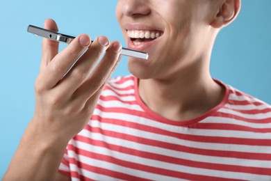 Young man recording voice message via smartphone on light blue background, closeup