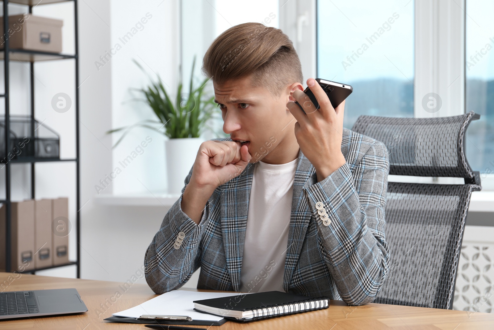 Photo of Young man with smartphone listening to voice message in office