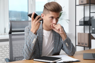 Photo of Young man with smartphone listening to voice message in office