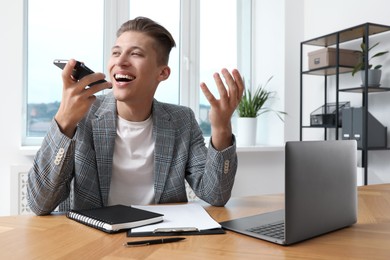 Photo of Young man recording voice message via smartphone in office