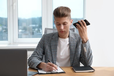 Photo of Young man with smartphone listening to voice message in office