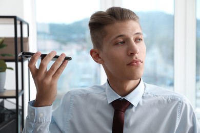 Photo of Young man with smartphone listening to voice message in office