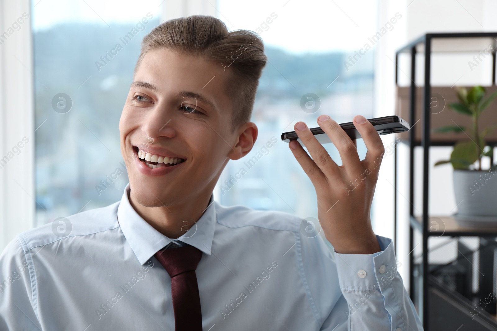 Photo of Young man with smartphone listening to voice message in office