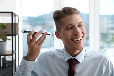 Young man with smartphone listening to voice message in office